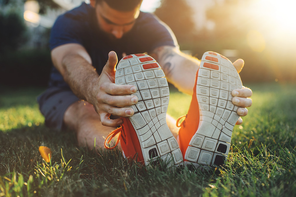 Man in shorts and a t-shirt stretches and holds his feet after running