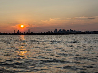Sunset over a city skyline with the sun reflecting on the water. The sky is orange and purple, creating a calm and serene atmosphere.
