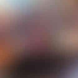 A group of people sit around a long table in a restaurant, enjoying a meal. Red cups, colorful plates, and warm lighting create a cozy atmosphere.