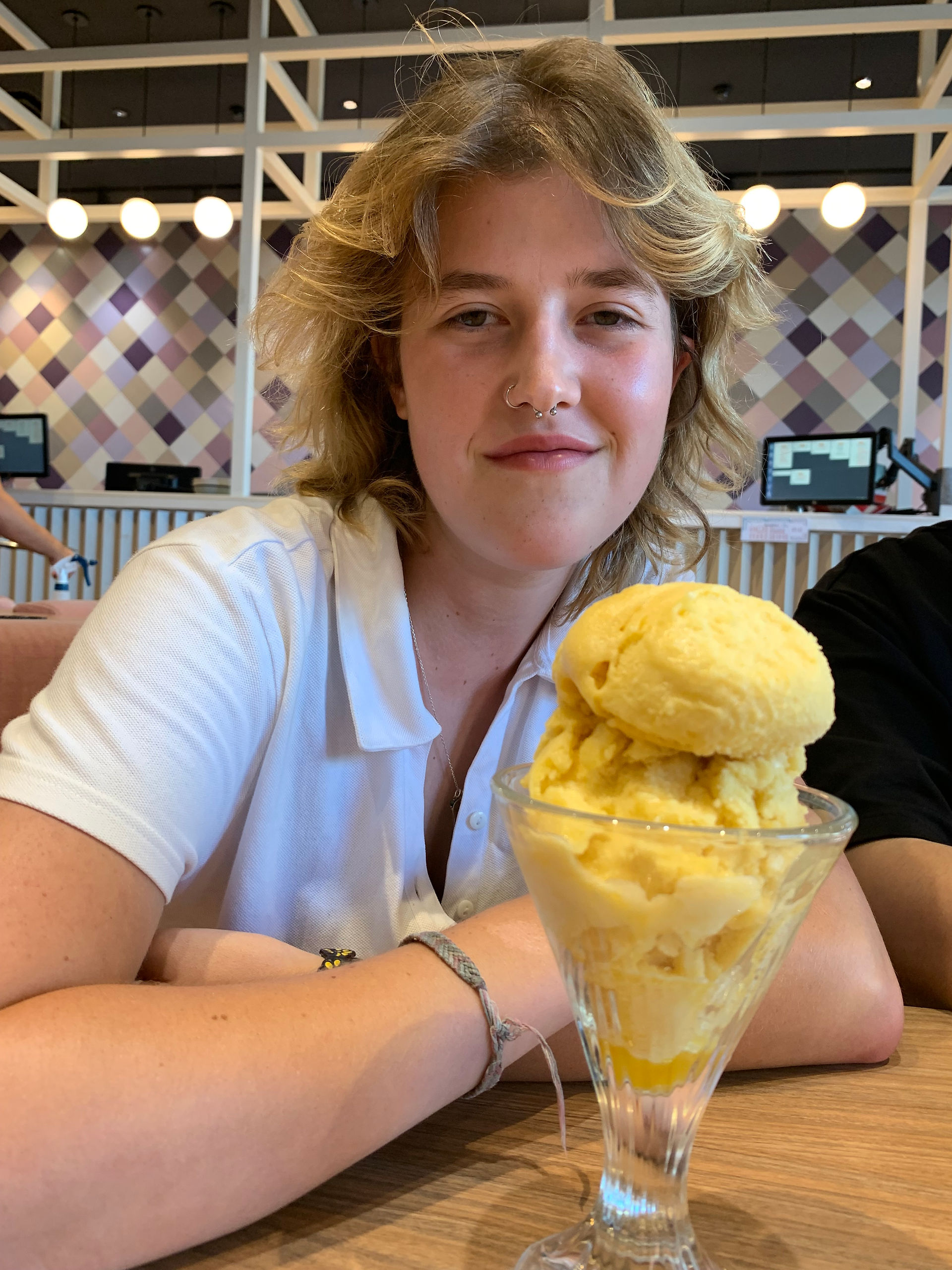 Girl smiling with yellow ice-cream in a glass. Wearing a white polo shirt.