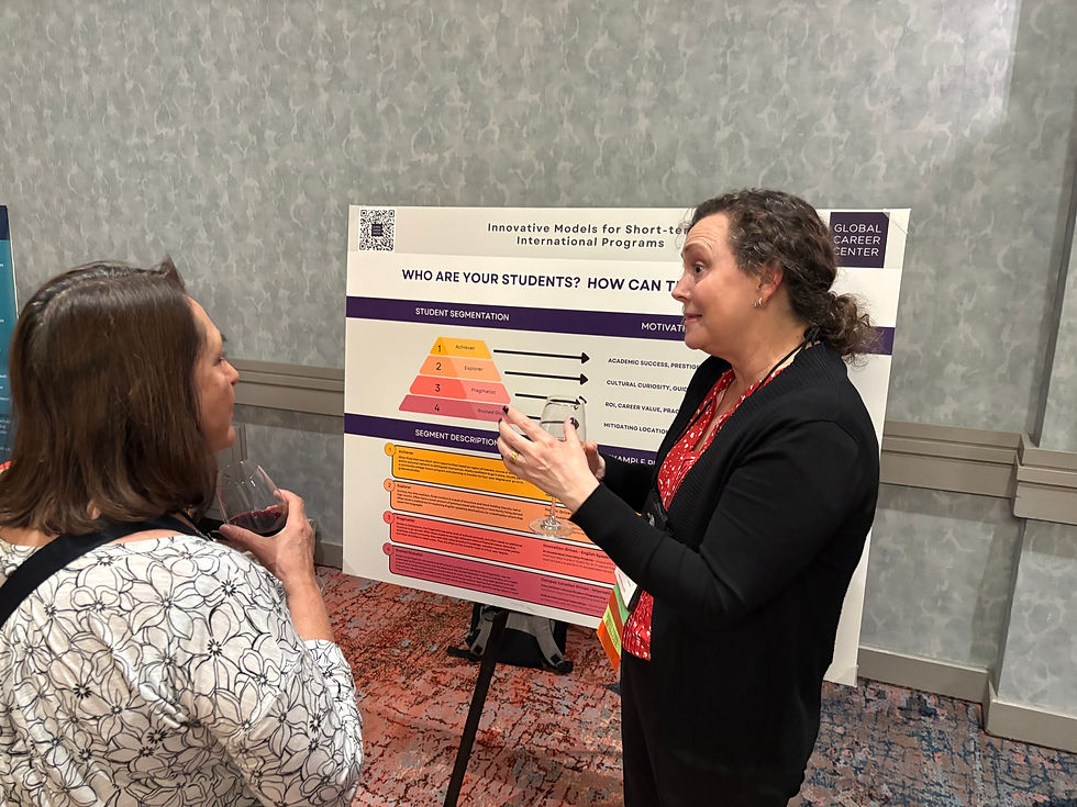 Two women discuss in front of a chart on student segmentation. One holds a glass of wine. The setting is a conference room with a patterned carpet.