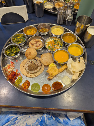 South Indian thali with curries, chutneys, breads and papad on a steel tray at a restaurant table, colorful and abundant