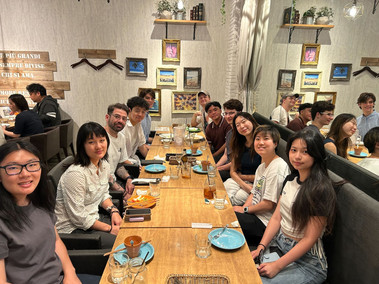 Group of people dining at a restaurant, plates, glasses and chopsticks visible. Casual attire.