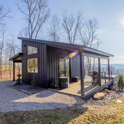 Modern black cabin with large windows on a sunny hillside.