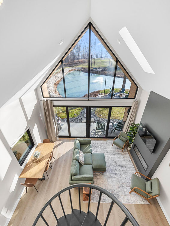 Modern A-frame living room overlooking pond through large triangular window.