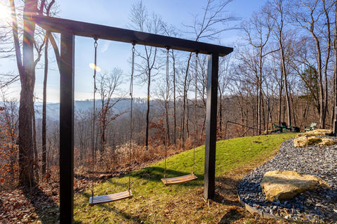 Wooden swing set overlooking a scenic, sunlit, forested valley landscape.