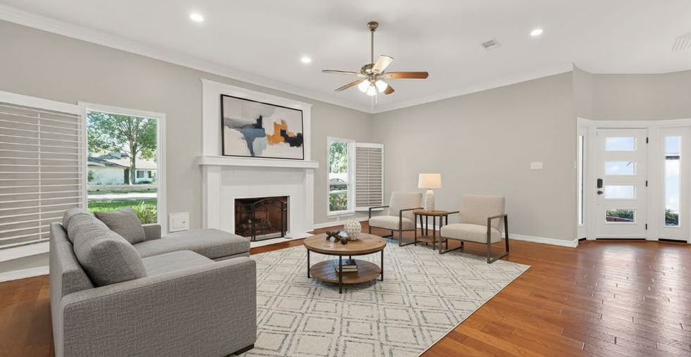 Open-concept living room with hardwood floors, large windows, crown molding, updated recessed lighting, neutral paint, and a statement fireplace in a fully remodeled Katy TX home.