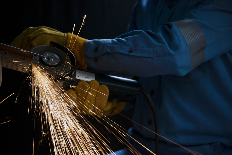 Trabajador de la industria portando overol ignífugo azul marca Texin FR con cortadora eléctrica sacando chispas.