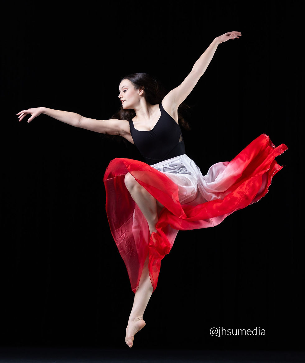 Woman dancing with arms lifted and one bent knee and one straight leg and wearing a red and white long skirt.