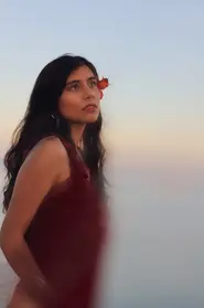 Beautiful South Asian female wearing a red summer dress in front of a hazy sunset backdrop.