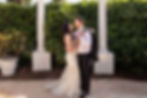 Couple in wedding attire posing between white columns