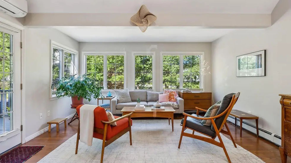 Cozy living room with mid-century furniture, large windows showing trees, a gray sofa, orange and gray chairs, and a soft, relaxing vibe.