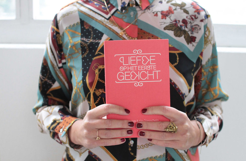 Persoon in kleurrijke blouse die een roze boek met titel vasthoudt