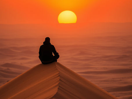 Hombre sentado en una duna alta descubriendo los secretos del desierto de Marruecos al atardecer.