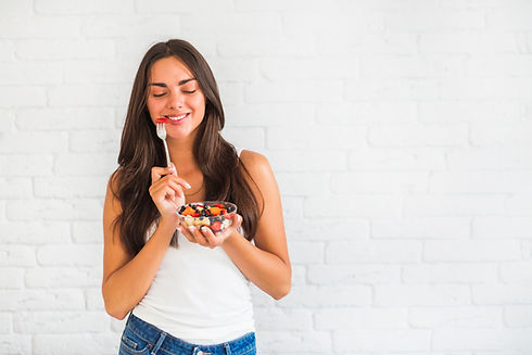 happy-young-woman-standing-against-white-wall-eating-fruit-salad.jpg