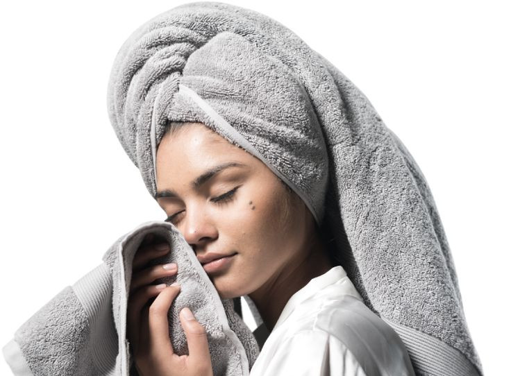 Woman with hair in a towel drying her face with a washcloth.