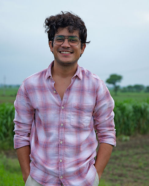 Candid outdoor portrait of the Fiction Is Real founder, smiling in a natural field setting, reflecting a warm, human, approachable creative spirit.