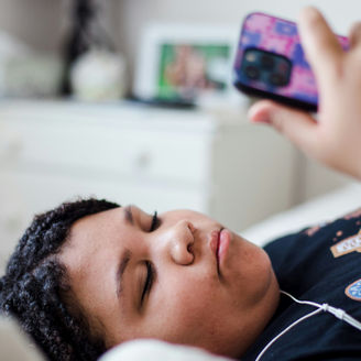 A teenager laying on a bed looking at their phone