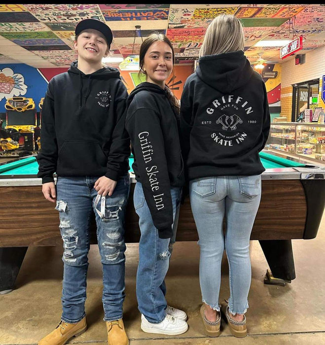 Three employees showing off branded hoodie with the griffin skate inn logo