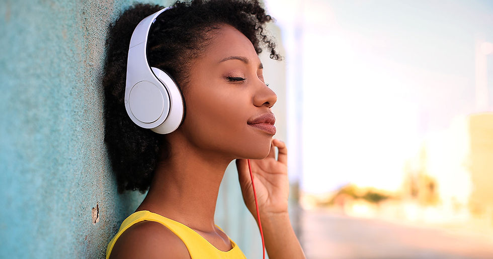 Uma mulher negra, com cabelos crespos e escuros, ouve música por um fone de ouvido branco.