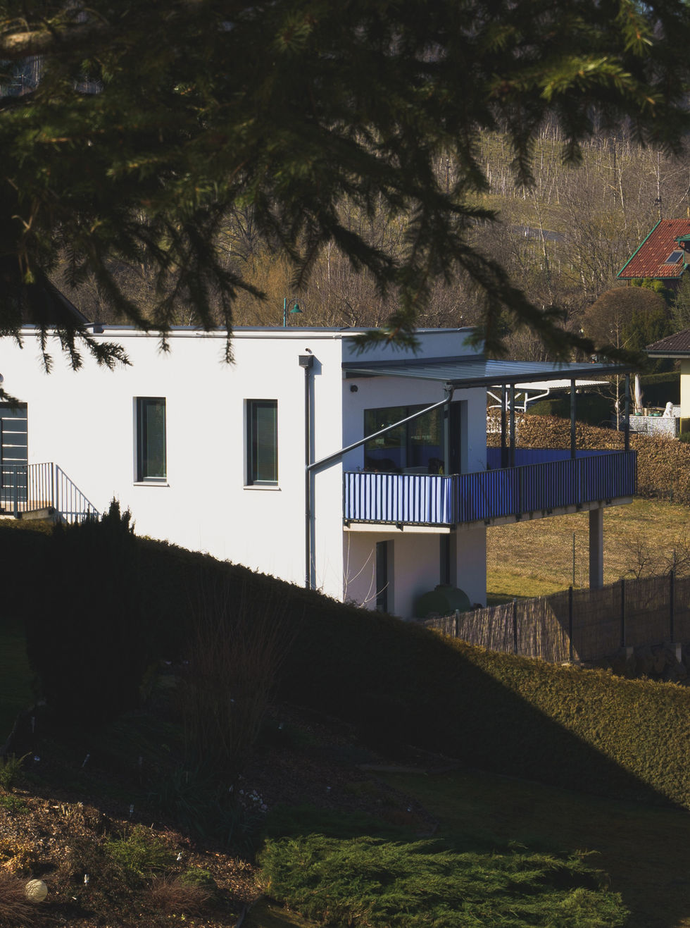 Ein weißes Haus fotografiert von weitem, es ist noch ein Balkon zu sehen.