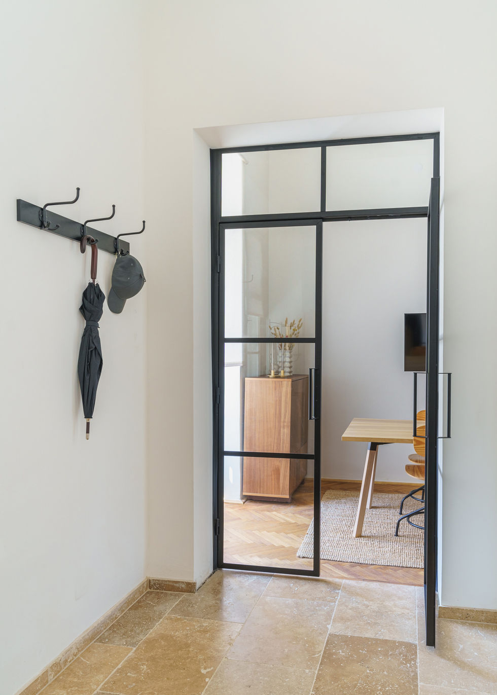 Der Gang einer Wohnung, auf den Hacken hängt ein Regenschirm und eine Kappe, eine Glastüre zeigt in den Nebenraum.