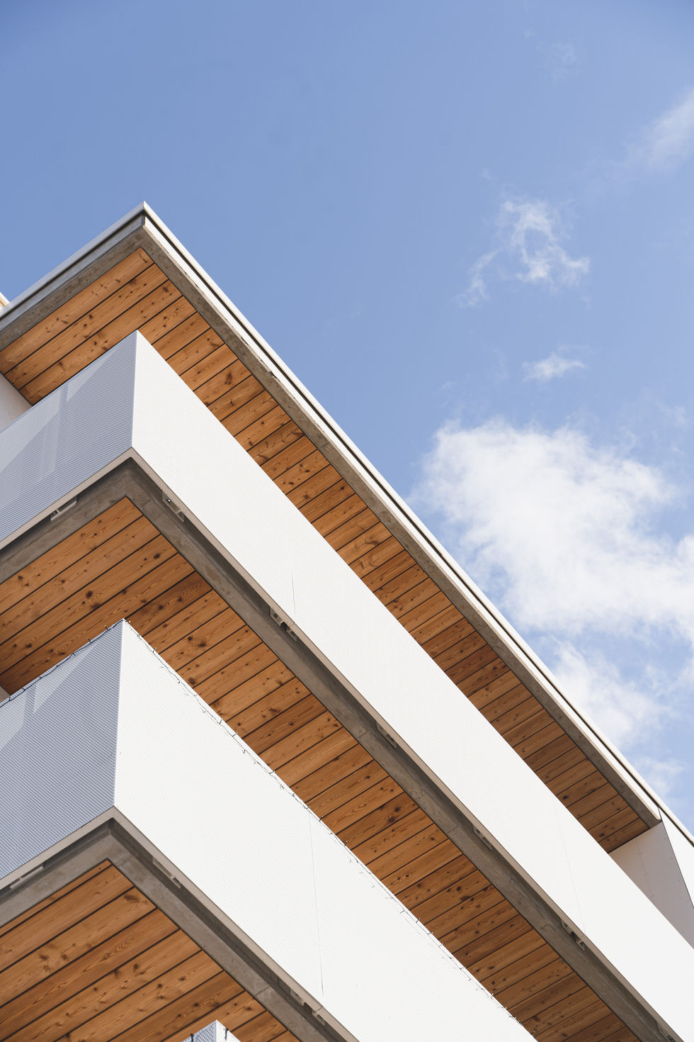 Ein Detail eines Wohnhauses, die Balkone sind von unten fotografiert, sodass die Linien des Balkons eine Diagonale über das Bild bilden.