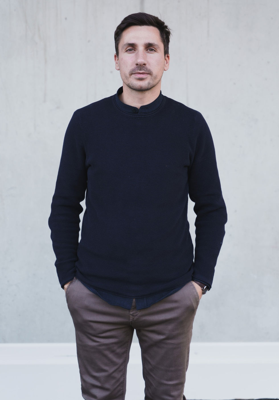 Ein Mann posiert vor einer Hauswand für ein Businessportait, er hält seine Hände in der Hosentasche und blickt direkt in die Kamera.