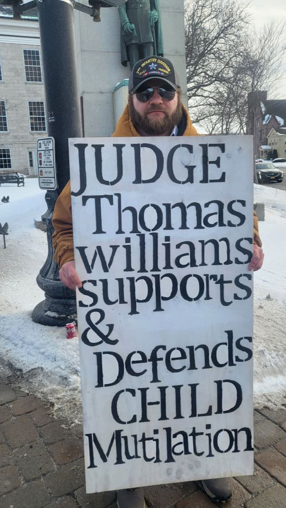 Ryan, holding a sign outside the court house before a proceeding after his child already received two shots of puberty blockers. 