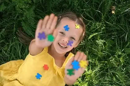 Laughing girl in the grass with colorful puzzle-piece stickers on her hands