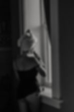 Woman in a black boudoir outfit standing by a window during a Niagara boudoir session photographed b