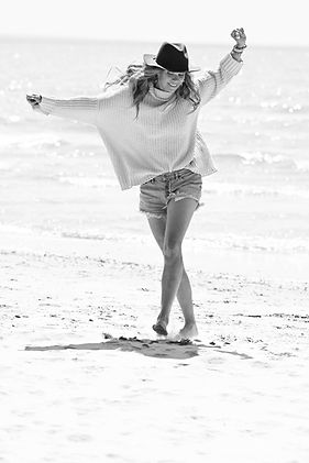 Black and white portrait of a woman in a hat and sweater walking on the beach, photographed for Haskell Photography’s 40 Over 40 portrait campaign.