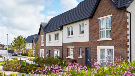 Cairn, Electrical Fit Out  by Greenlight, Residential Development – Row of modern two-storey semi-detached homes with red brick and cream render facades, black tiled roofs, and landscaped front gardens featuring flowering shrubs and neatly maintained pathways.