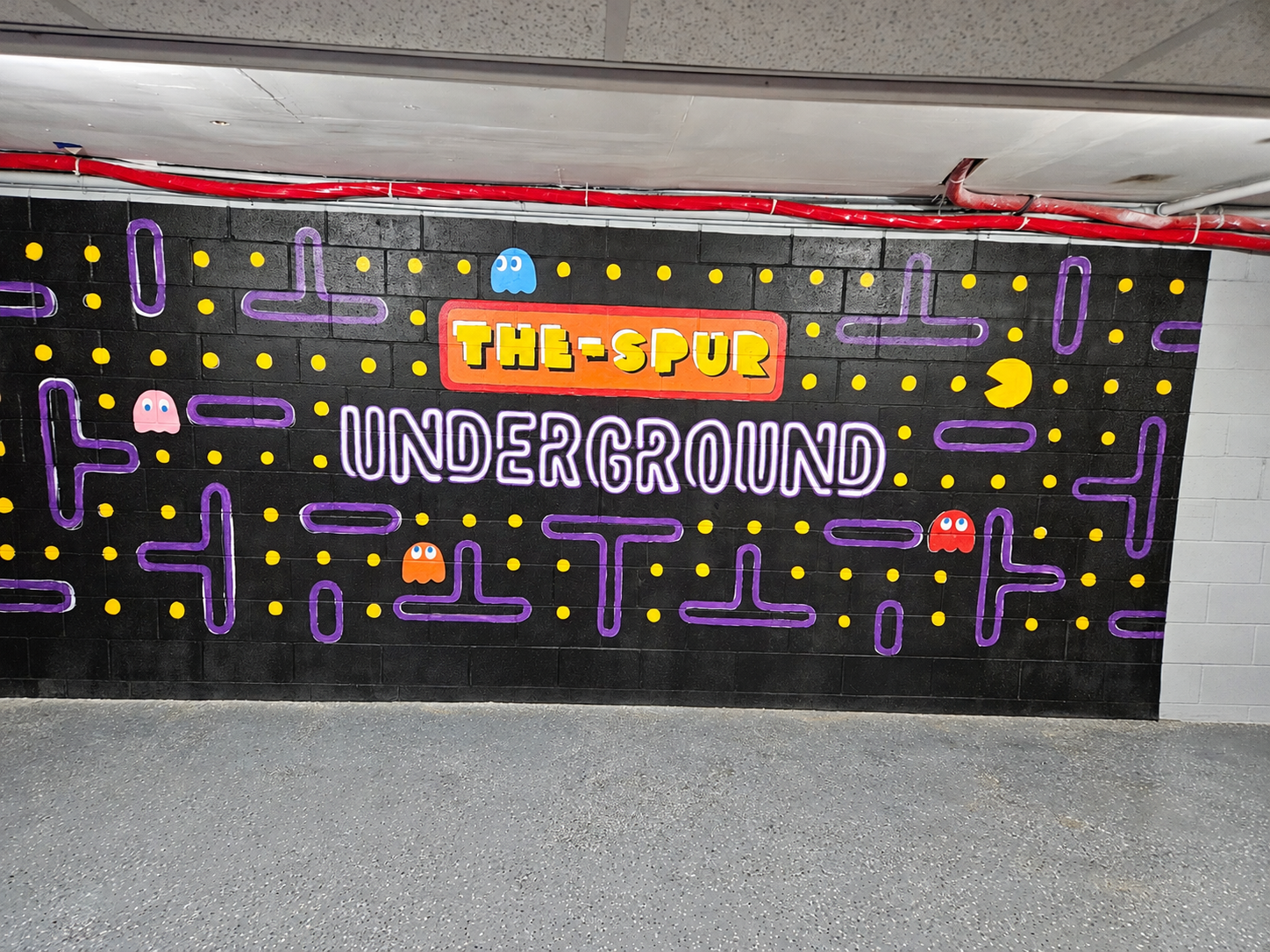 The Spur Underground hand-painted arcade mural by Leah Stephens, featuring colorful ghosts, yellow dots and purple maze paths