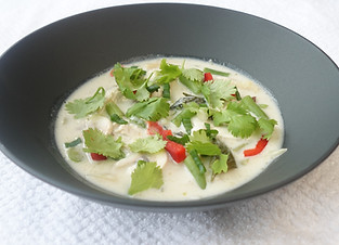 Bowl of creamy Thai chicken and Coconut soup with green beans, mushrooms and red peppers, topped with cilantro and green onions. The black bowl rests on a white textured surface.
