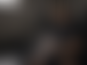 Middle-aged man seated in an industrial gym calmly applying chalk to his hands, with soft natural light and a light dusting of chalk particles in the air, and open space on the left side of the frame.