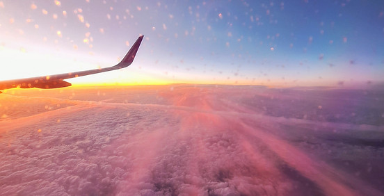 Widok z okna samolotu na różowy zachód słońca nad chmurami podczas lotu na Islandię.