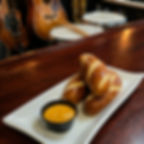 Pretzel rolls with cheese dip on a white plate at a bar, with violin, guitar, and drums in the background