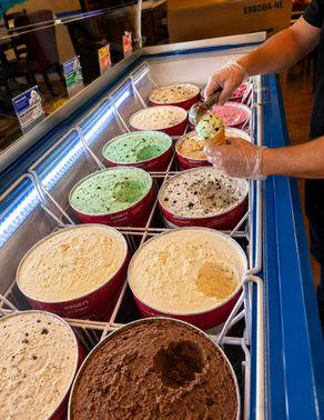 Hersey's Ice cream tubs in a freezer, showing green mint, vanilla, cookies, and chocolate flavors under blue lights.