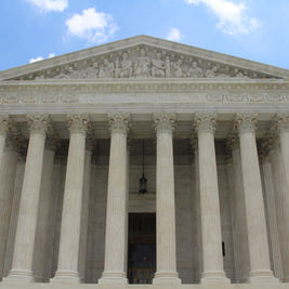 U.S. Supreme Court facade with tall marble columns, the words Equal Justice Under Law, and a guard on the steps under a blue sky.