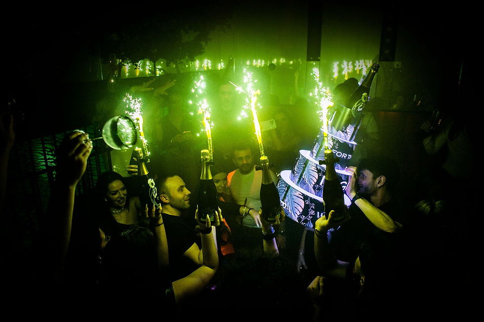 Waiters carrying champagne bottles for a table client in a nightclub while a promoter watches.