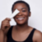 Femme souriante tenant un tube de crème cosmétique.