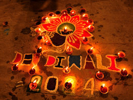 An intricate colorful rangoli design illuminated by glowing earthen oil lamps (diyas) for Dev Diwali celebrations in Varanasi, India.