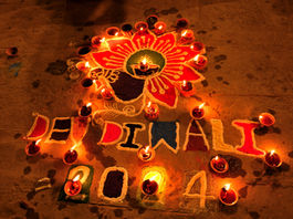 An intricate colorful rangoli design illuminated by glowing earthen oil lamps (diyas) for Dev Diwali celebrations in Varanasi, India.