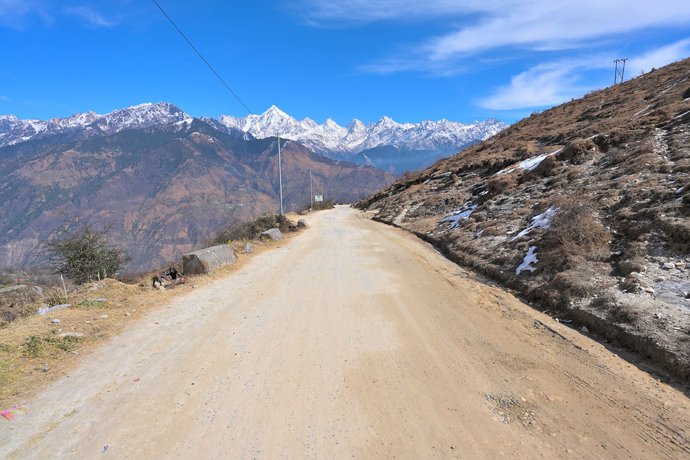 An unpaved mountain road leads along the ridge with the Panchachuli range rising across the horizon.