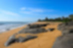 Scenic view of Kodi Beach in Bekal, Kasaragod, Kerala, India, featuring large rocks, towering coconut trees, and gentle waves lapping against the golden shoreline, creating a peaceful coastal landscape. Shot on Nikon Z8.