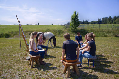 Jana Schöpper und Simone Krebs sitzen vor einer Gruppe. Szenerie ist draußen, grüne Wiese, Sommer. SaddleUp Coaching - Business Coaching, Fpührungskräfteentwicklung.