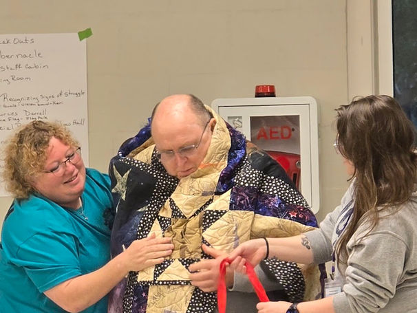 Two women help a man put on a quilt