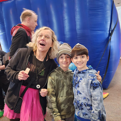 Woman in pink tutu with students in front of a large "bounce house"