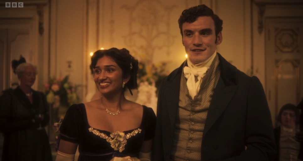 Smiling couple in formal 19th-century attire at a candlelit ballroom; BBC logo in top left.
